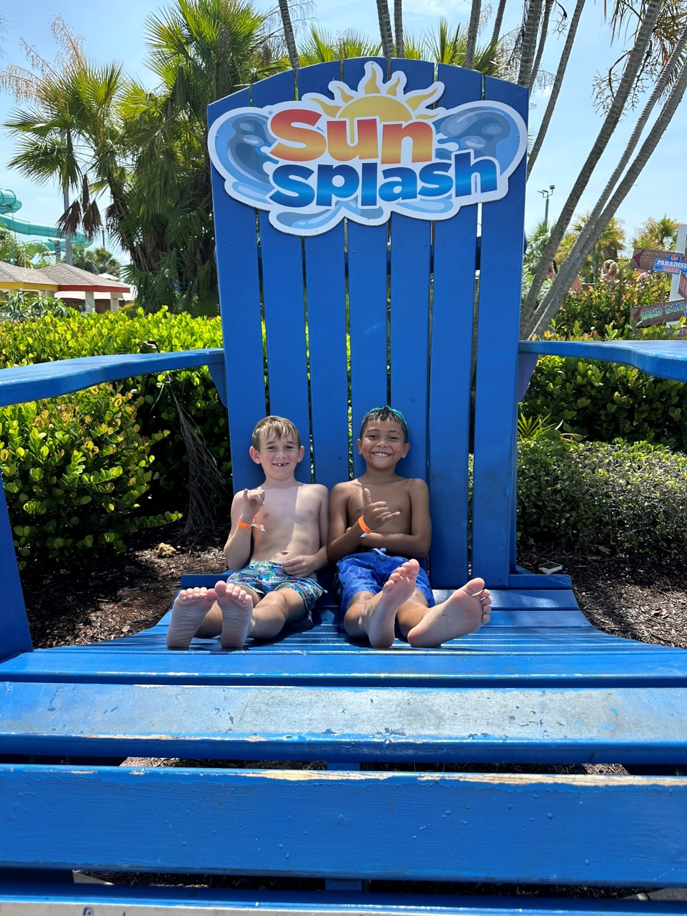 Two boys in swim trunks relax barefoot on an oversized blue SunSplash chair at SunSplash Waterpark